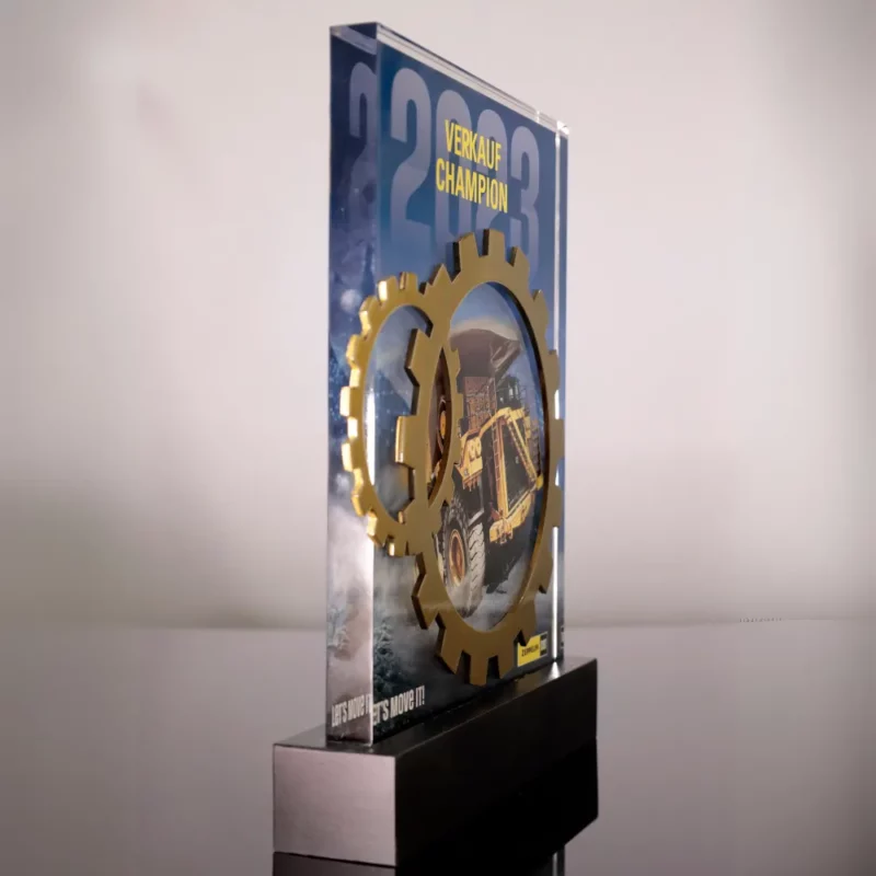 A modern glass award featuring golden gear elements and the title 'Verkauf Champion 2023' with construction imagery.